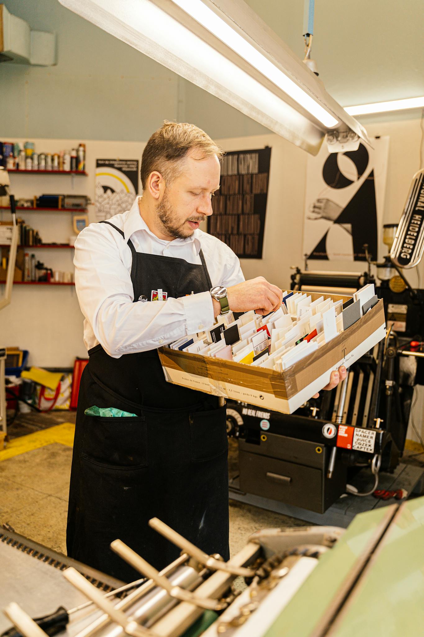 Adult man organizing cards in an industrial print workshop, wearing apron and focused on work.