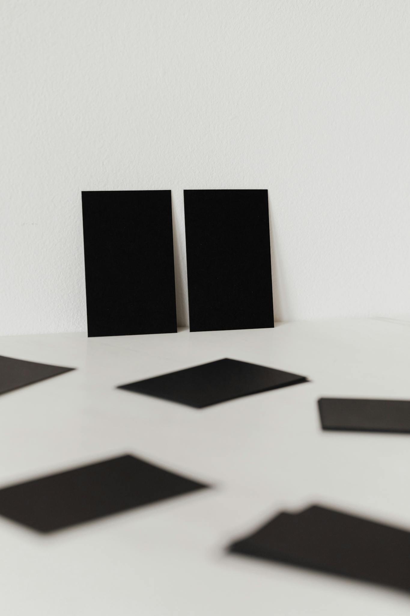 Collection of black mockup business cards placed against white wall and scattered on white surface